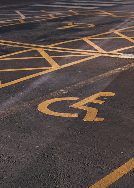 A tall metal parking restriction sign mounted on a pole stands in front of a stone wall beneath a window with a yellow-painted frame. The sign displays two sections: the upper section indicates no par